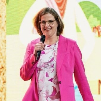 Mocha Shmigelsky on stage with a microphone, in a hot pink suit